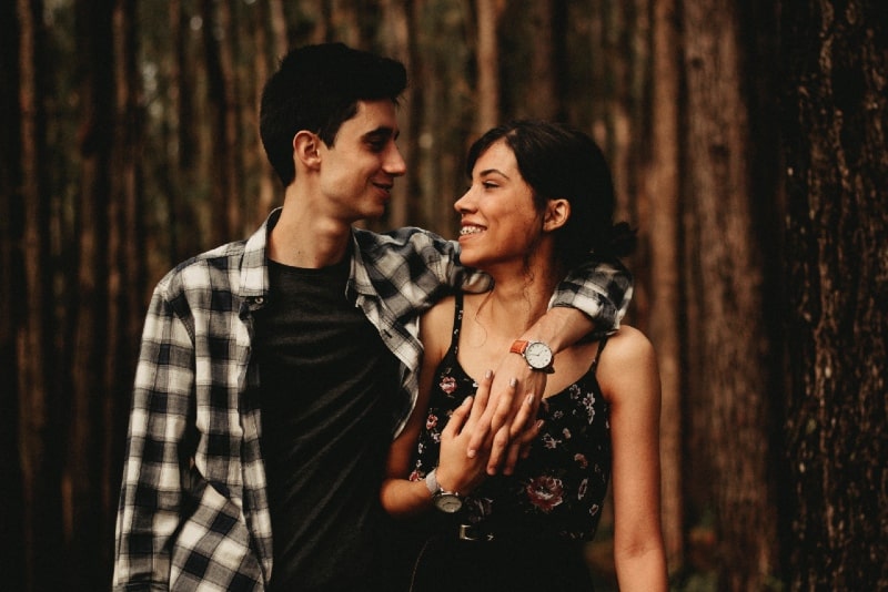man hugging woman while standing in forest