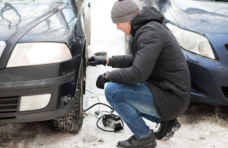 uomo che gonfia un pneumatico d'auto sgonfio durante la stagione della neve