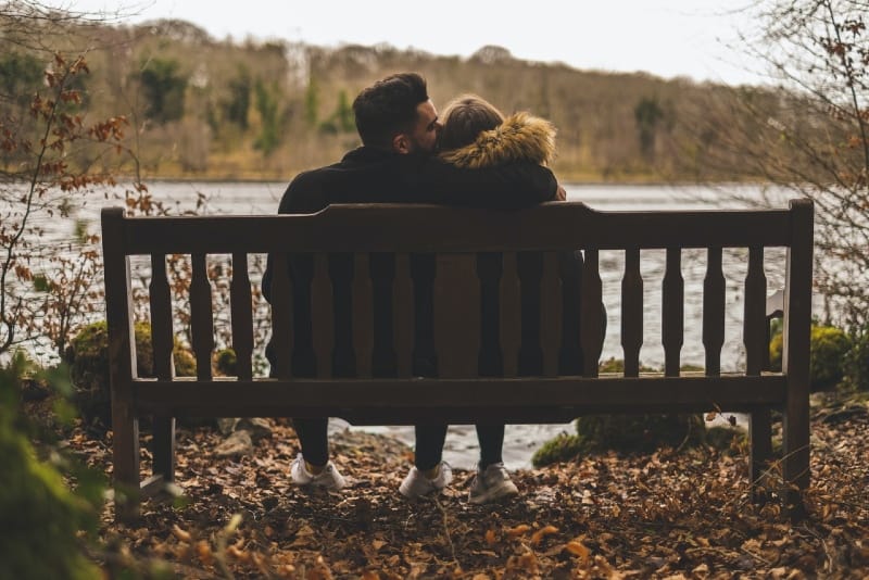 uomo che bacia la testa della donna mentre è seduto su una panchina