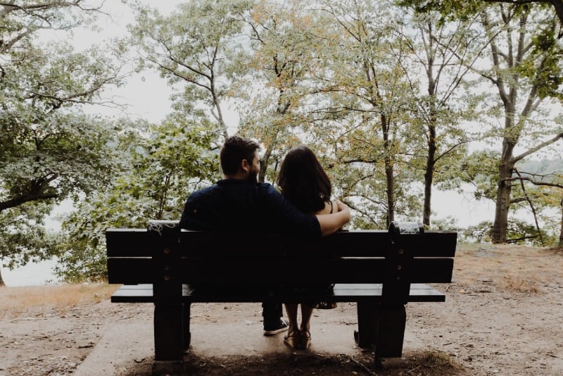 man looking at woman while sitting on brown wooden bench