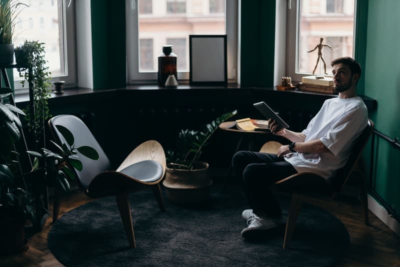 man on ipad sitting inside the room near the windows