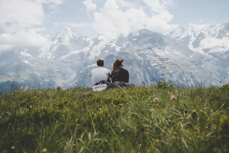 man sitting beside woman on grass facing mountain