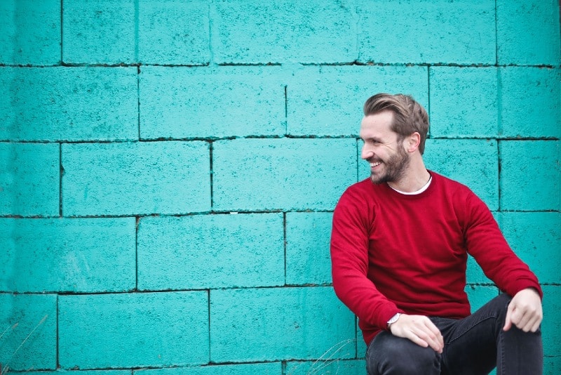 man in red sweatshirt sitting near blue wall
