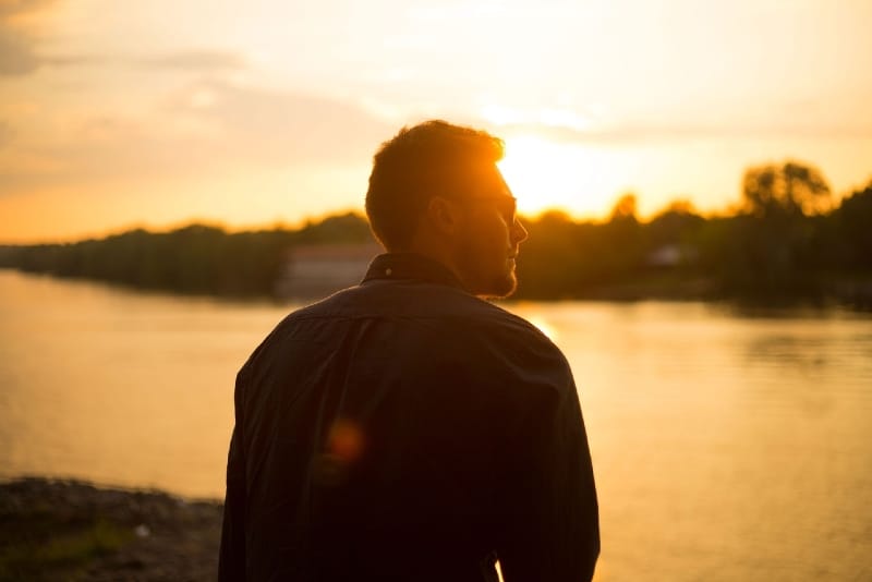hombre sentado cerca del agua durante la puesta de sol