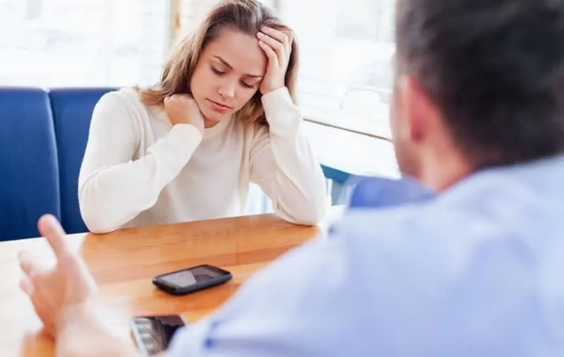 not happy woman sitting in front of a man in a table with a phone on top of the table
