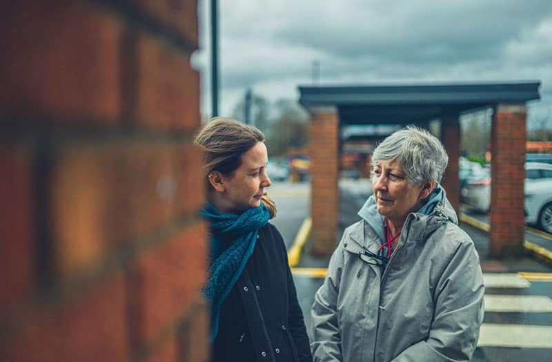 uma mulher idosa e uma senhora a conversar no parque de estacionamento