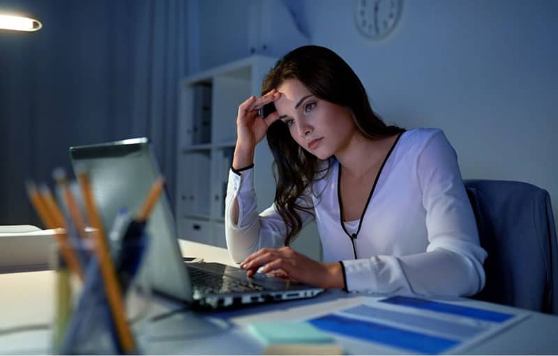 Donna pensierosa di fronte al computer portatile in ufficio di notte