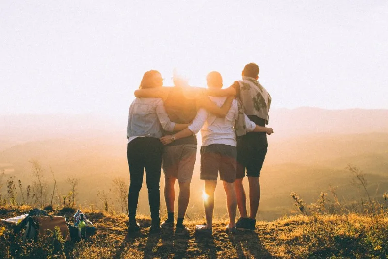 four people hugging while looking at sunset