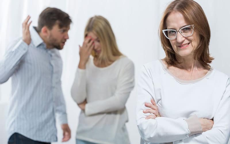 picture of a mean nosy mother smiling amidst marital conflict of a couple at her back