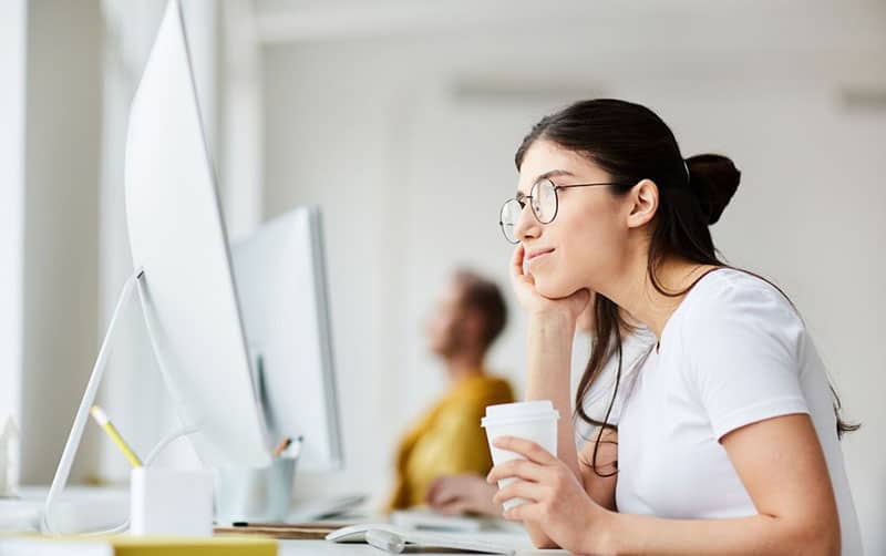 picture of a woman daydreaming inside the office while facing her computer