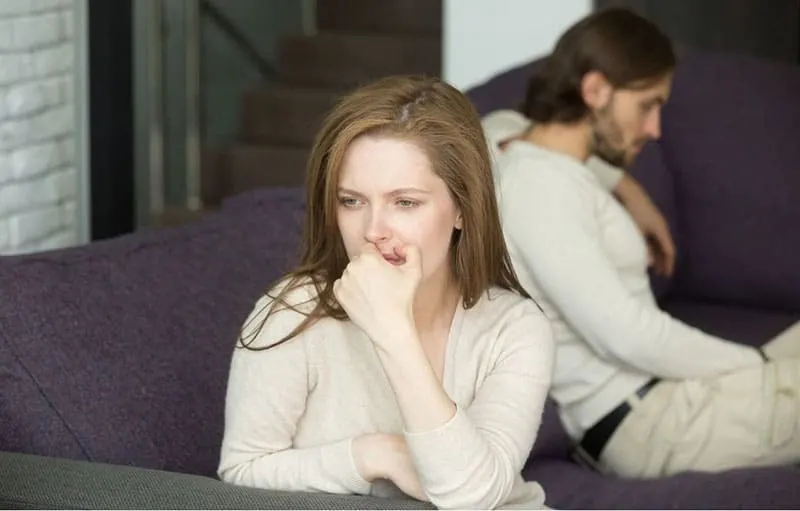 sad disappointed woman thinking and sitting on sofa far from a man sitting on the same sofa