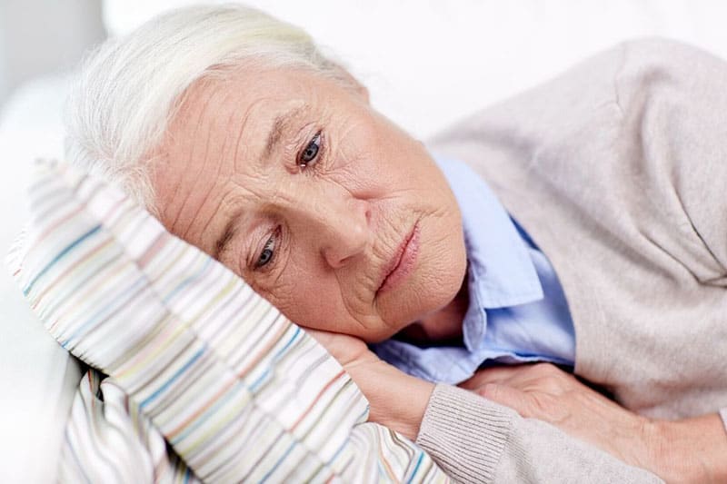 sad senior woman lying on pillow at home