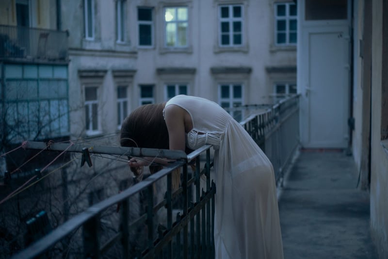 sad woman head down leaning on the railings wearing nighties