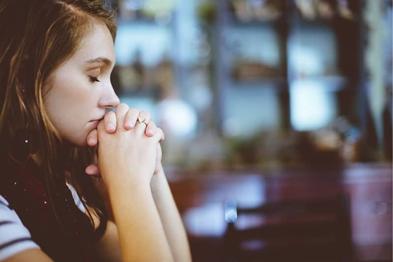 vista laterale di una donna che prega con il pugno chiuso vicino alla bocca