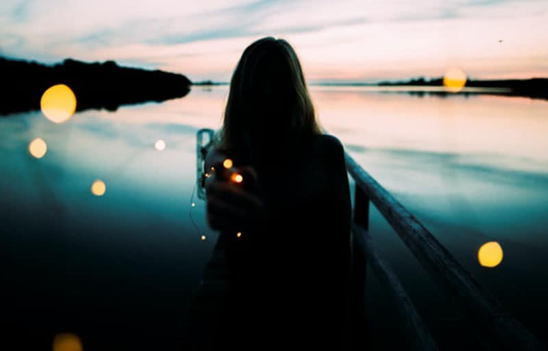 silhouette of woman leaning on the railings facing the body of water