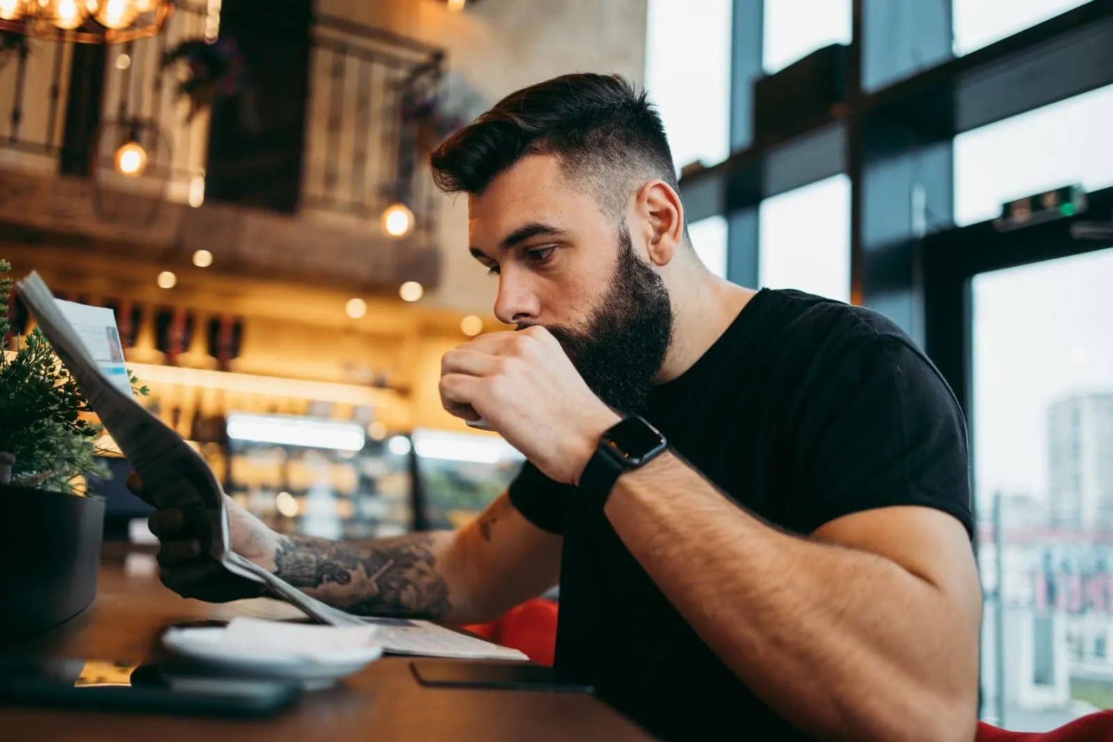 tattooed man sitting in cafe drinking coffee