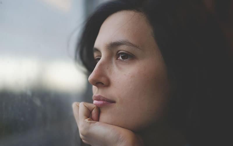 mujer pensativa mirando al exterior a través de las ventanas con la mano apoyando la cabeza