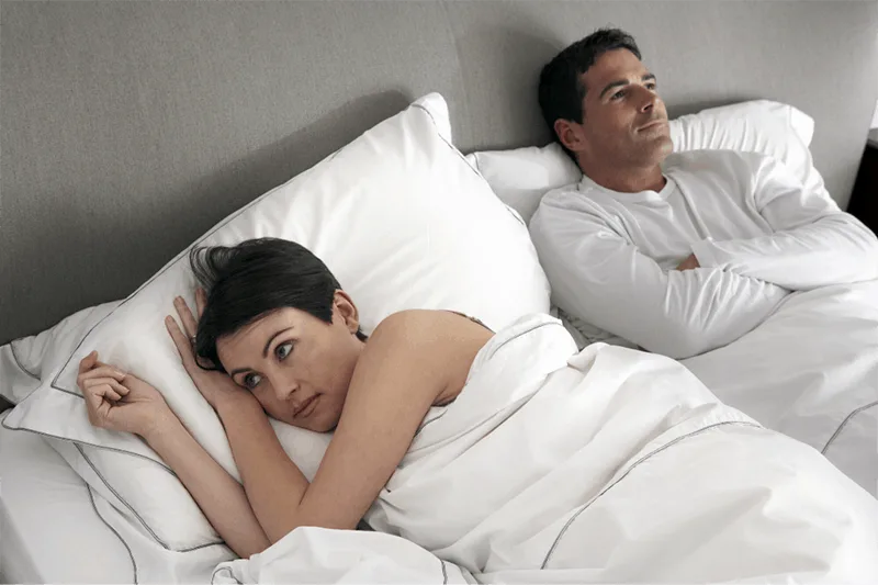 unhappy couple lying on bed with woman in white linen bed