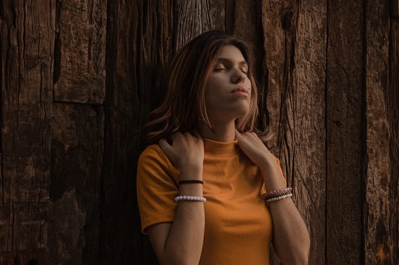 upset woman leaning against an old wooden wall wearing orange turtleneck top