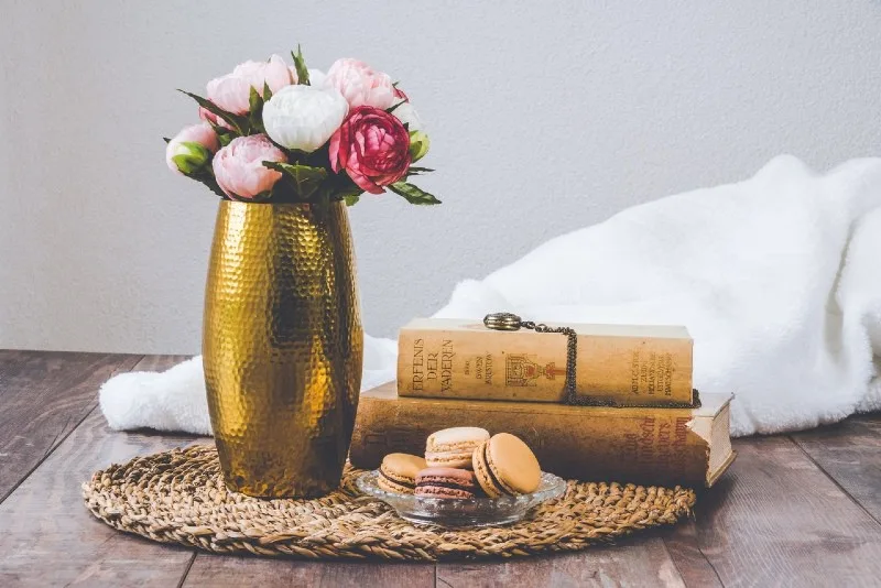 golden vase with flowers on floor near books