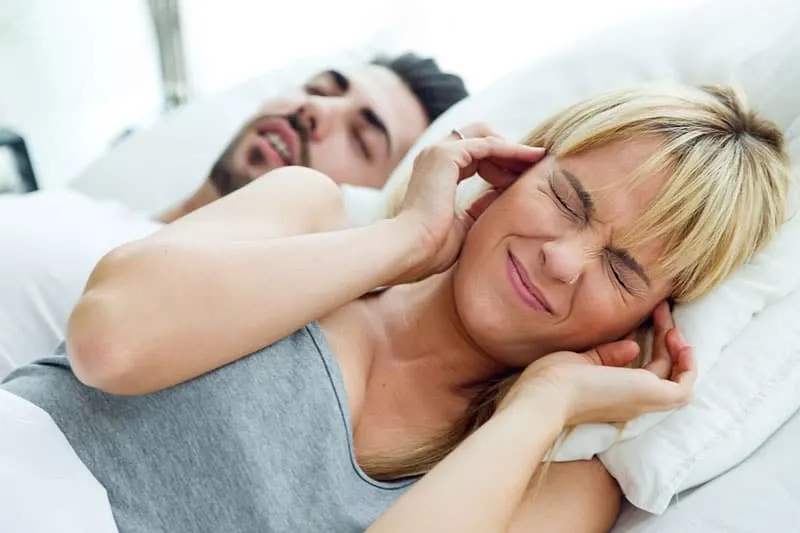 wife covering ears getting annoyed by the man snoring while sleeping beside her
