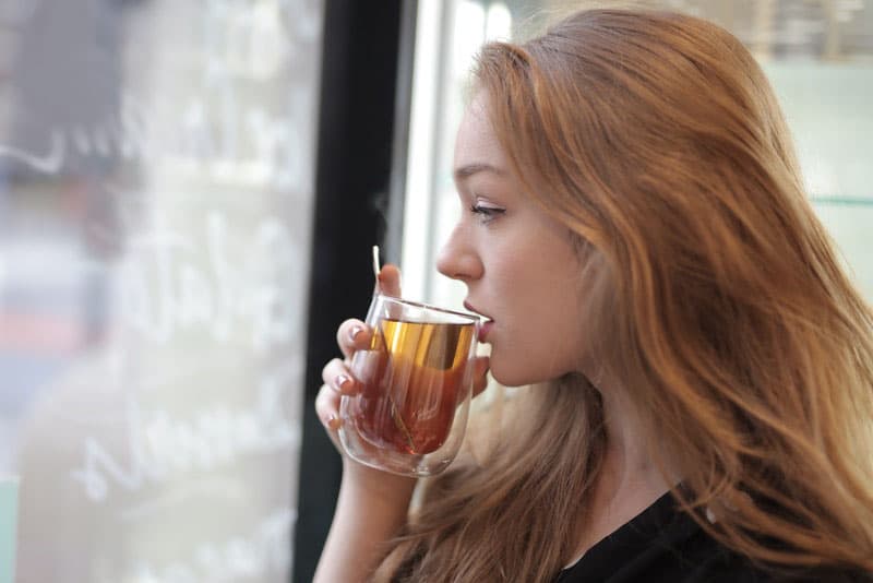 mujer a punto de beber té en una taza de té de pie cerca de la ventana de cristal