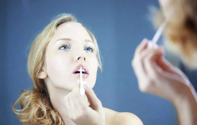 woman applying lipstick facing the mirror