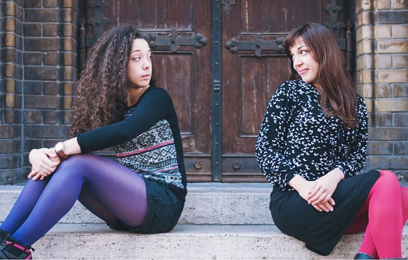 woman asking for forgiveness to another lady sitting on the stairs near the door