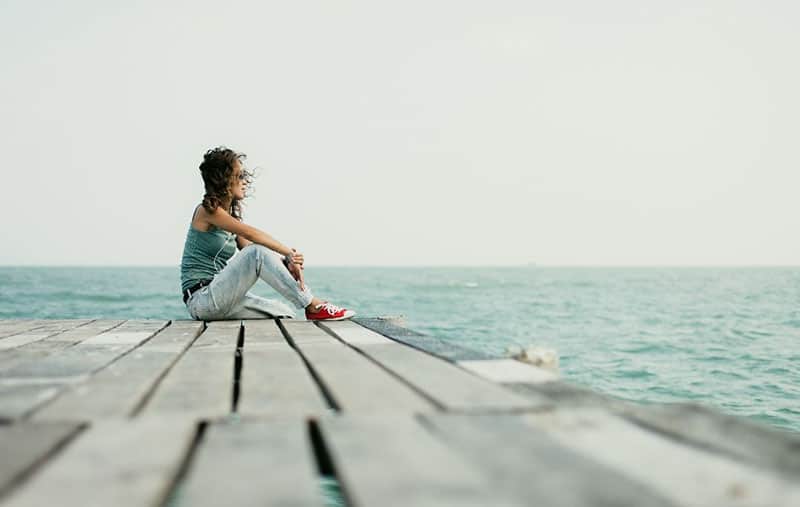 woman by the sea sitting on wooden platform wearing sneakers