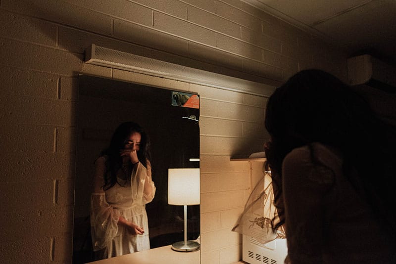 woman crying in front of the mirror wearing a night gown inside the the bath room