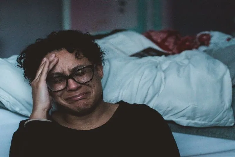 woman in black top crying while sitting near bed