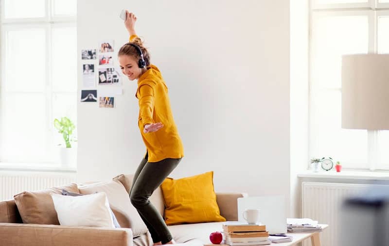 mujer baila sola encima del sofa dentro del salon