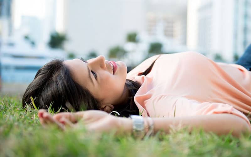 woman daydreaming lying on the green grasses near buildings