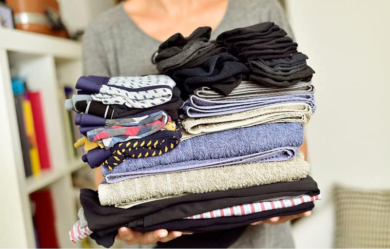 woman declutters wardrobe with a pile of clothes on hand