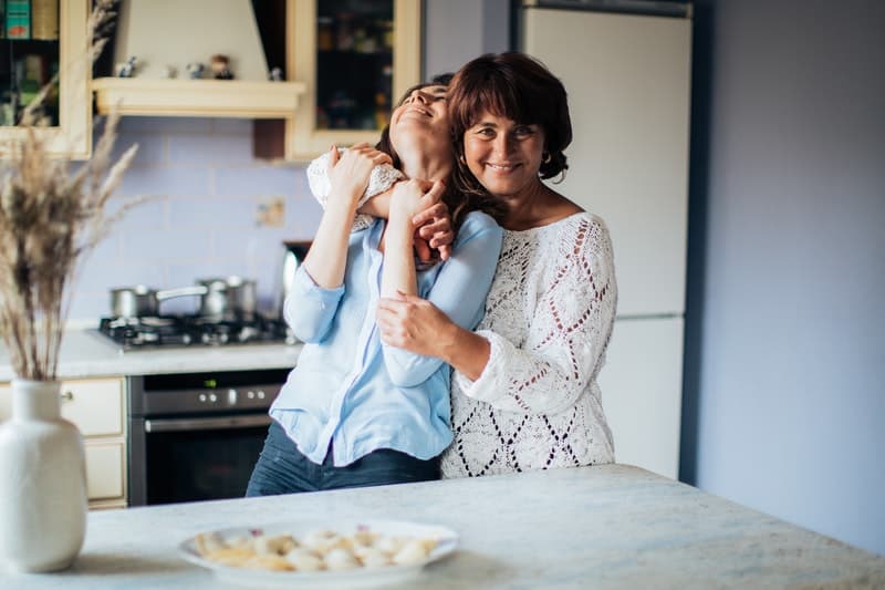 mulher abraçada à sua mãe na cozinha 