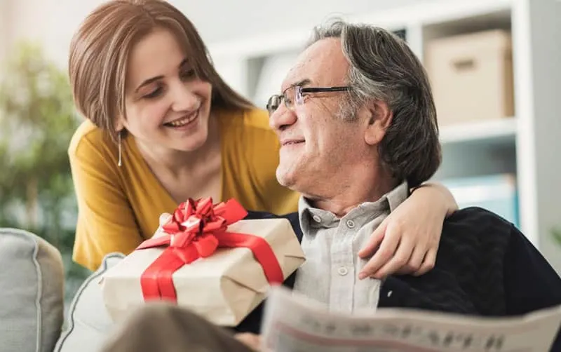 woman giving gift to a senior man sitting on a couch
