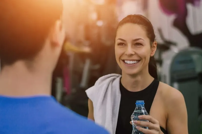 smiling woman holding bottle of water while looking at man