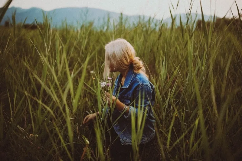 blonde woman holding flowers while standing in the field