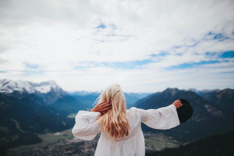 woman in white dress holding hat looking at mountain