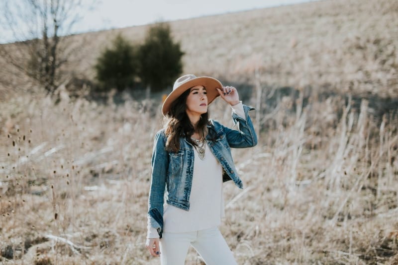 donna con giacca di jeans che tiene il cappello in un campo