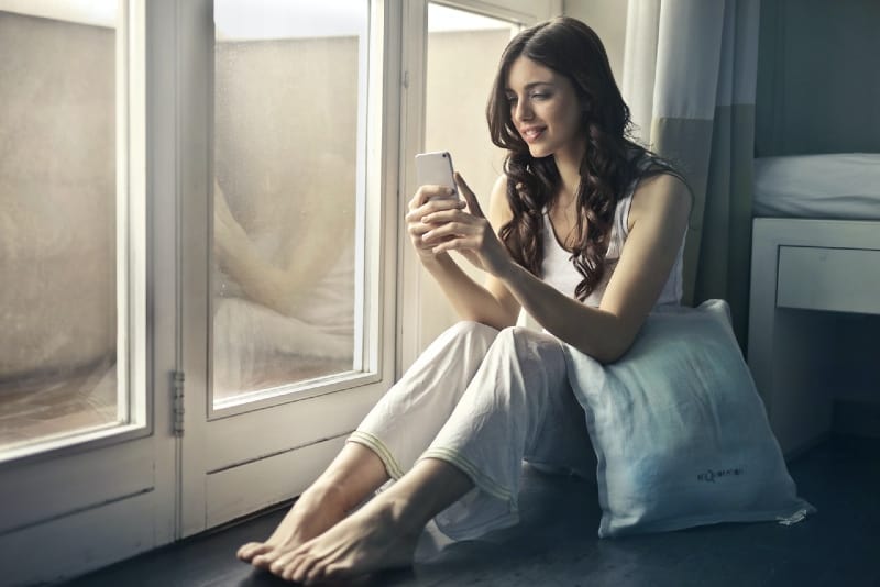 mujer sentada junto a la ventana y con el teléfono en la mano