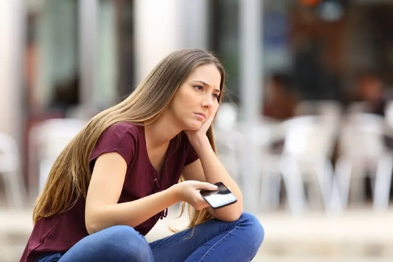 sad woman holding phone while sitting outdoor