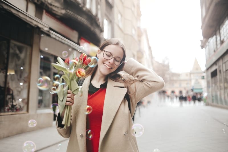 smiling woman in brown coat holding bouquet of tulips
