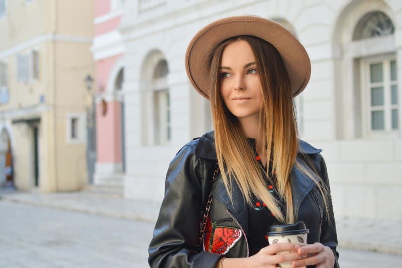 mujer con sombrero sosteniendo vaso de plástico de pie al aire libre