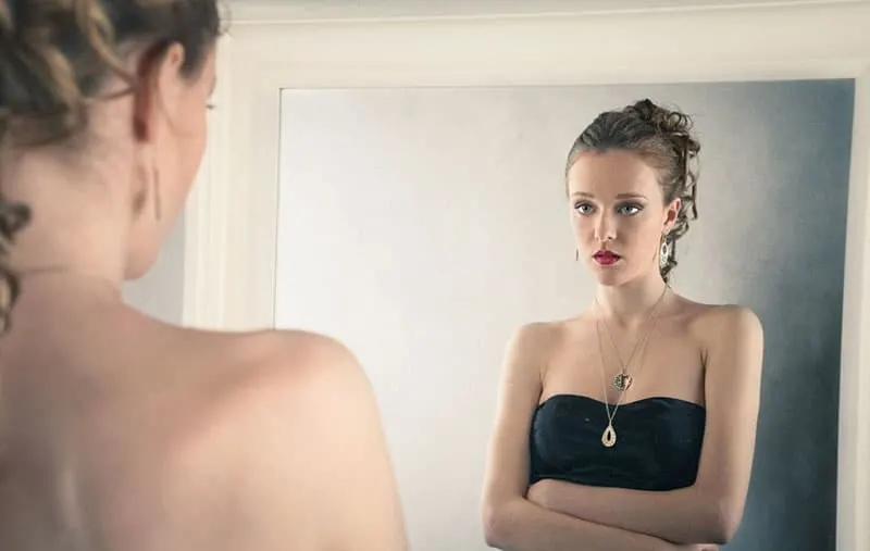 woman in black dress facing the mirror looking sad