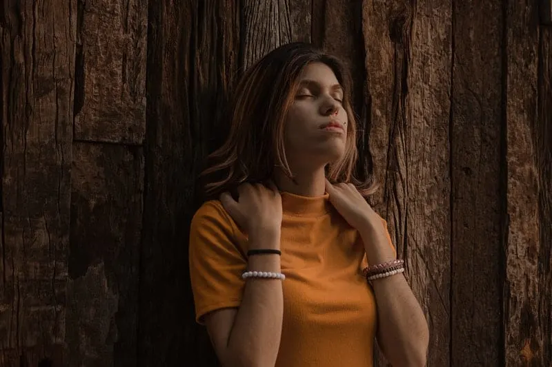 woman in orange turtleneck shirt leaning on a brown wooden wall
