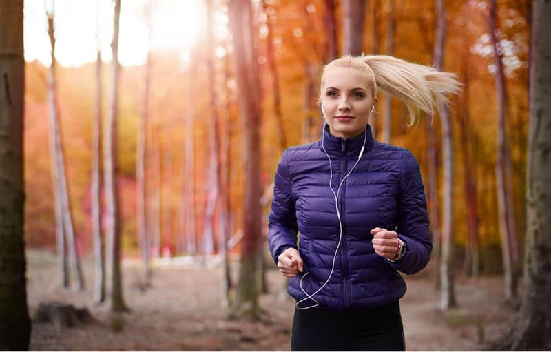 donna che fa jogging nel bosco mentre ascolta la musica con gli auricolari