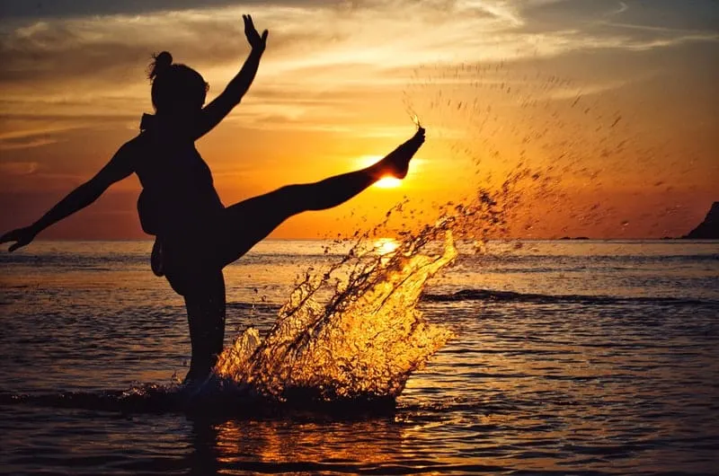 woman kicks water during sunset/sunrise in silhouette