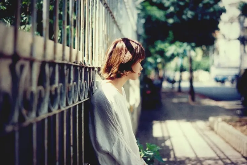 sad woman in white top leaning on fence