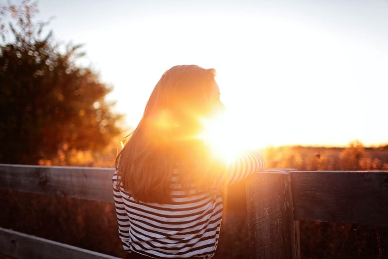 woman in striped shirt leaning on wooden fence